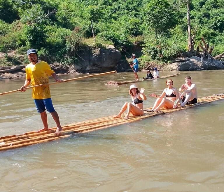 Guests sit on a bamboo raft on the Mae Wang River with a guide standing at the front